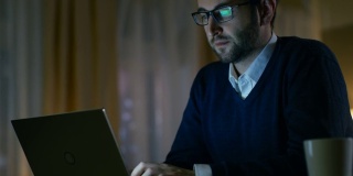 在家的中年男子戴上眼镜，开始在笔记本电脑上工作。背景是他的黄色风格公寓。