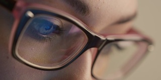 近距离拍摄的女人眼睛在眼镜反射一个工作的电脑屏幕。