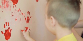 快乐可爱的小男孩在墙上留下他的红色手印玩得很开心。这个快乐的孩子的特写。母亲和孩子的概念。Slowmotion。