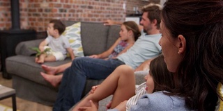 一家人坐在开放式休息室的沙发上看电视
