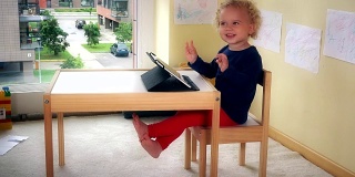可爱的孩子坐在桌子旁边的小椅子上玩平板电脑。