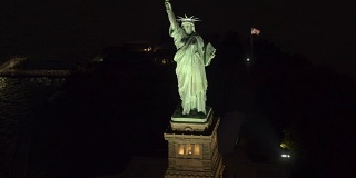 空中特写:著名的自由女神像在夜晚被点亮，在黑暗中闪闪发光