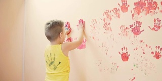 快乐可爱的小男孩和他年轻的妈妈在墙上留下五颜六色的手印玩得很开心。年轻的幸福的家庭。母亲和孩子的概念。Slowmotion
