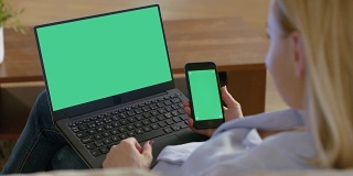 肩上的一个女人使用笔记本电脑和拿着智能手机，都有模拟绿色屏幕。