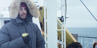 穿着保暖外套的冒险家站在船上，用无线电通信。这是下雪和刮风
