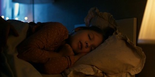 甜美的小女孩晚上睡在她的床上，她的妈妈盖好她的毯子。