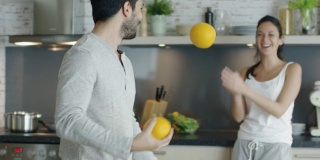 一个活泼的年轻人用厨房里的橙子杂耍来打动他的女朋友。