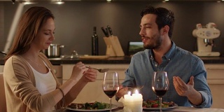 一对美丽的夫妇在厨房里吃烛光晚餐。他们吃喝聊天。两个都有好心情和微笑很多。结束运动。
