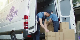 两个强壮的送货员装载满硬纸板箱的商业车辆。