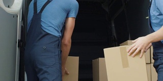 两名强壮的送货员慢动作装载商业车辆的硬纸盒。