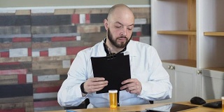 一个30岁的秃顶胡子医生坐在他的医疗室办公室里，在一张全高清的桌子中间