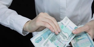 一名女子迟疑地数着钱，一叠一叠的钞票变成了一个图像，俄罗斯卢布
