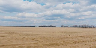 一辆快速行驶的汽车窗外的景色。早春耕地，蓝天白云。农业用地。POV 3轴稳定视频