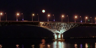 满月从桥上升起。延时。俄罗斯萨拉托夫和恩格斯之间的公路桥。伏尔加河。夜晚的车灯和街灯。4 k,超高清