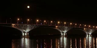 满月从桥上升起。延时。俄罗斯萨拉托夫和恩格斯之间的公路桥。伏尔加河。夜晚的车灯和街灯。4 k,超高清
