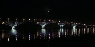 满月从桥上升起。俄罗斯萨拉托夫和恩格斯之间的公路桥。伏尔加河。夜晚的车灯和街灯。4 k,超高清