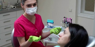 一位戴着面罩和手套的牙医向他的女病人解释即将进行的治疗准备检查。在4 k拍摄