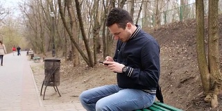 一名男子坐在公园长椅上玩手机