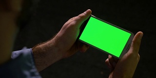 男人用绿色屏幕的智能手机看媒体内容