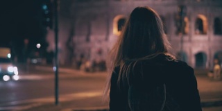 后视图的深色头发的女人走在深夜在罗马，意大利。女孩在斗兽场附近的人行横道上过马路