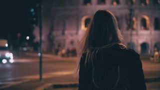 后视图的深色头发的女人走在深夜在罗马，意大利。女孩在斗兽场附近的人行横道上过马路视频素材模板下载