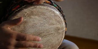 一个男人的手在一个非洲皮肤覆盖的手鼓上敲出一个节拍。