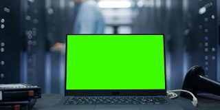 桌上放着一台绿色屏幕的笔记本电脑。在服务器机架行和IT工程师工作的后台数据中心。
