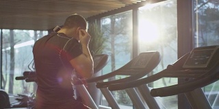 一个健壮的运动员戴着耳机开始在体育馆里的跑步机上跑步。