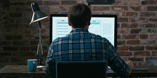 年轻的设计师坐在阁楼的显示器前，在平板电脑上画草图。