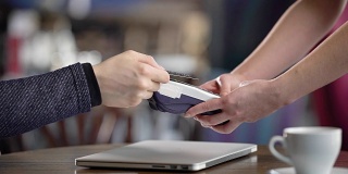 在咖啡厅使用信用卡终端。特写，男性的手拿着信用卡。无联系方式付款