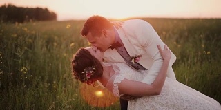 英俊的新郎把他美丽的新娘抱在怀里，亲吻她。日落时分在一个美丽的地方举行婚礼