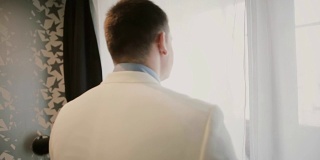 一个穿白色西装的年轻人走近窗户。新郎准备结婚的日子。早上仪式之前