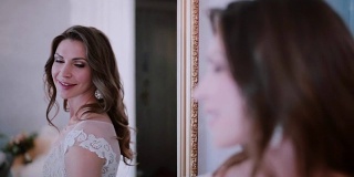 年轻的新娘站在镜子前，然后转身看着镜头。女人在结婚前看自己的倒影