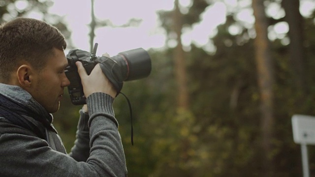 一位男性摄影师正在秋天的森林里拍照。