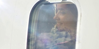在飞行过程中，年轻女子透过飞机窗户望出去，脸上露出微笑。