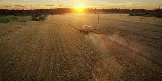 无人机拍摄的联合收割机在日落时分在田里工作。