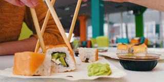 一个女孩和一个男孩坐在寿司吧里，拿着木制的寿司棒