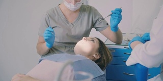 计划牙科检查。在医生治疗病人时，一个女人张着嘴坐在牙医的椅子上