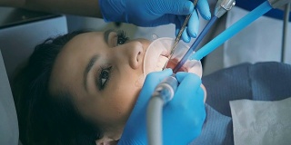 牙医拿起牙科器械，转向病人。医生和护士对牙齿进行清洁和抛光
