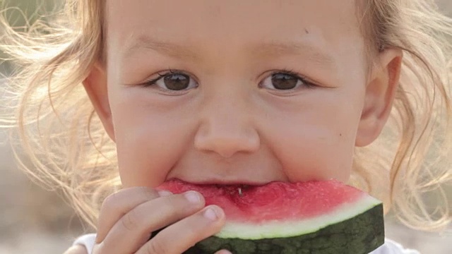 小可爱的小女孩在日出时吃红西瓜的特写