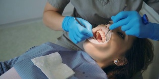 一位年轻女子在看牙医。女性躺在牙科椅上，医生在擦拭她的牙齿