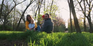 快乐的家庭在公园春天。父母和两个女儿坐在一起，玩耍