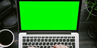 俯视图男性双手工作的笔记本电脑与绿色屏幕在白色的桌子上从上方