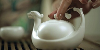 女性用手在茶壶杯里泡茶。用茶壶泡茶的特写