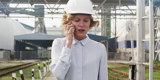 在工业环境中戴安全帽走路和打电话的女人