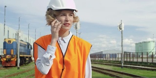 戴安全帽、穿安全背心的妇女在火车站边走边讲电话。