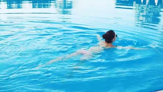 在一个阳光明媚的夏日里，穿着比基尼、戴着墨镜的黑发女子走进游泳池游泳视频素材模板下载