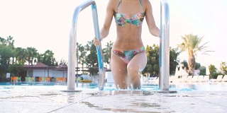 年轻的黑发女人穿着比基尼和太阳镜在阳光明媚的夏天从游泳池出来