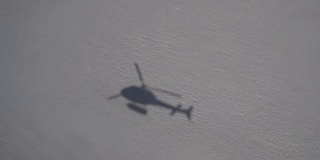 直升机阴影在雪地上空飞行