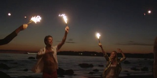 一群快乐的年轻人手里拿着闪闪发光的烟花在海滩上奔跑